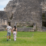Couple exploring ancient Mayan ruins in Belize, walking together through historic stone pyramids during a Belize couples vacation, surrounded by lush tropical scenery.