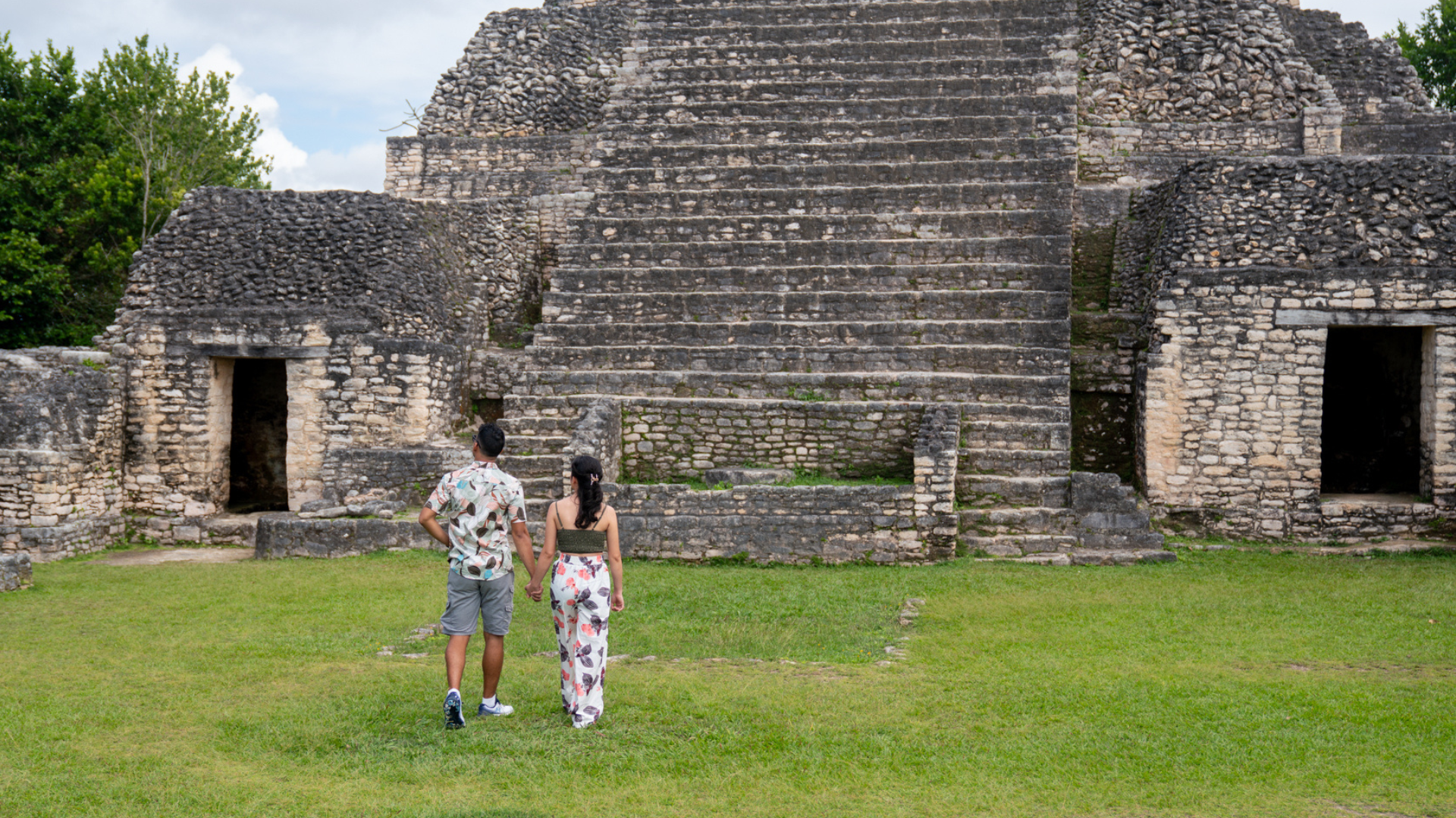 Couple exploring ancient Mayan ruins in Belize, walking together through historic stone pyramids during a Belize couples vacation, surrounded by lush tropical scenery.